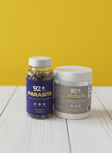 Load image into Gallery viewer, 92+ Parasite Cleanse and Zeolite bottles on a wooden surface with a green blurred background.
